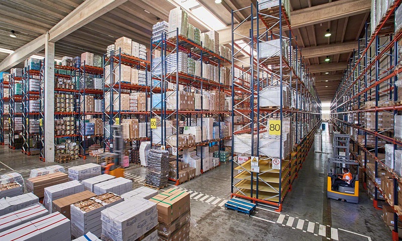 Warehouse with a lot shelves and some goods on the ground and forklift